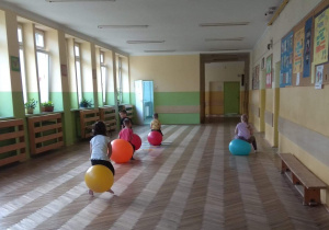 Dzieci skaczą na piłkach po szkolnym korytarzu.