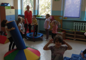 Dzieci bawią się na sali zabaw. Chłopiec skacze na małej trampolinie.