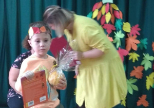 Chłopiec odebrał nagrodę dla swojej grupy: dyplom, dynię i książeczkę.