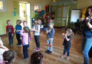 Dzieci pokazują umówione ruchy do melodii piosenki wygrywanej przez panią na skrzypcach.