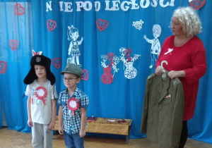 Pani pokazuje żołnierski mundur, dzieci przymierzają żołnierskie czapki.