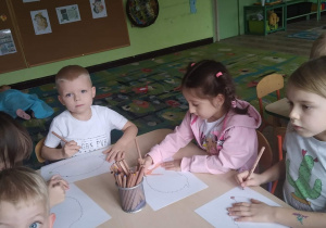 Dzieci siedzą przy stole i kolorują jeża.