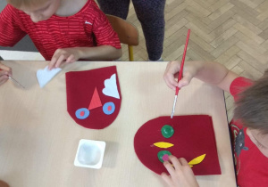 Dzieci układają i przyklejają elementy ozdobne do szablonu pacynki.
