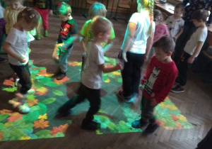 Dzieci na magicznym dywanie zmiatają nogami liście.