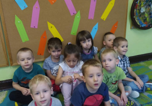 Dzieci siedzą przy tablicy z kolorowymi kredkami.