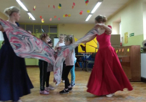 Dzieci wraz z tancerkami próbują zatańczyć wspólny taniec z szarfą.