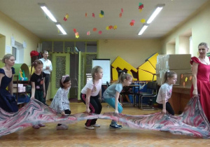 Dzieci wraz z tancerkami wykonują układ taneczny z szarfą.