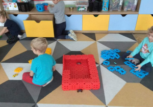 Dzieci na dywanie układają budowle z nowych klocków.