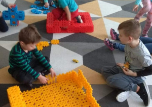 Dzieci na dywanie bawią się klockami.