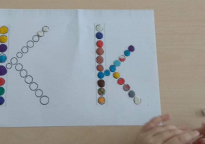 Dziecko wykleja szablon małej i wielkiej literki "k, K" kulkami plasteliny.