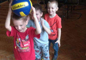Chłopcy stojąc jeden za drugim, podają sobie piłkę nad głową.