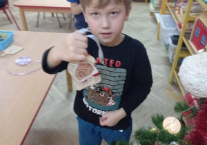 Chłopiec prezentuje własnoręcznie wykonaną ozdobę choinkową.