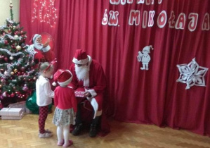 Dziewczynki wręczają św. Mikołajowi laurkę i ciasteczka