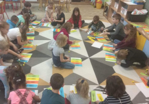 Dzieci siedzą na dywanie i układają w odpowiedniej kolejności kolorowe kartki z drzewami. Kolory symbolizują pory roku.