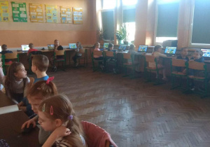 Dzieci siedzą przy komputerach w sali informatycznej.