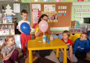 Chłopiec trzyma balon napompowany powietrzem, pani trzyma balon, który pompuje reakcja chemiczna, wynikła z połączenia sody i octu.