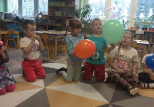 Dzieci trzymają balony nadmuchane przez siebie ustami.