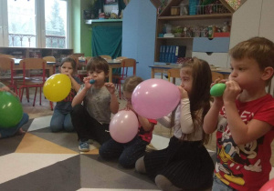 Dzieci pompują balony ustami.