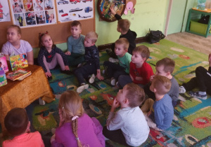 Dzieci siedzą na dywanie i słuchają czytanej przez rodzica bajki.
