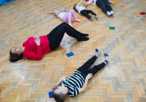 Dzieci z mamami ćwiczą na podłodze.