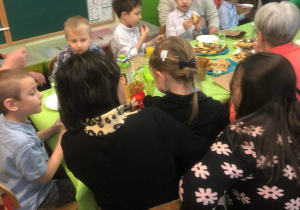 Dzieci wraz z zaproszonymi gośćmi siedzą przy stole.