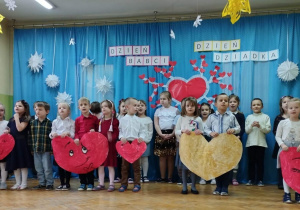 Dzieci trzymając szablony serc, deklamują wiersze dla swoich Babć i Dziadków.