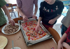 Dzieci układają składniki na pizzy.
