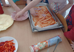 Dzieci układają składniki na pizzy.