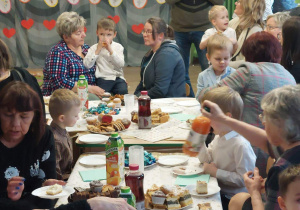 Dzieci wspólnie z babciami i dziadkami jedzą wspólny poczęstunek.