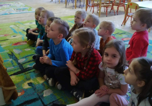 Dzieci siedzą na dywanie i uważnie słuchają bajki.