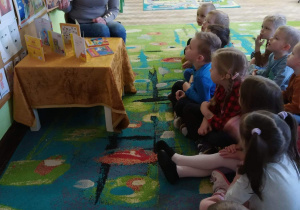 Dzieci siedzą na dywanie i słuchają bajki o zygzaku.