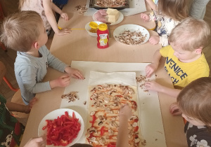 Dzieci nakładają czerwona paprykę na pizzę.