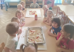 Dzieci przygotowują pizzę do pieczenia.