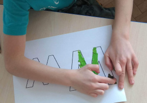 Chłopiec maluje plasteliną, wypełniając kontur litery W.