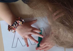 Dziewczynka maluje plasteliną, wypełniając kontur litery W.