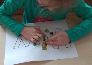 Dziewczynka maluje plasteliną, wypełniając kontur litery W.