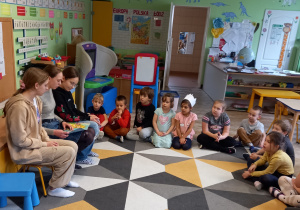 Dzieci słuchają bajek czytanych przez uczennice ze szkoły.