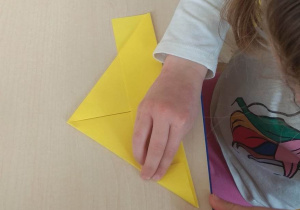 Dziecko wg instrukcji nauczyciela składa kartkę papieru, by powstała łódeczka.