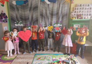 Dzieci stoją w półkolu i pokazują swoje czerwone serduszka.