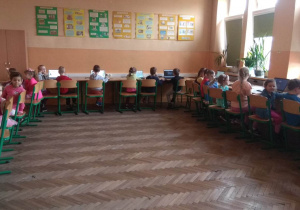 Dzieci w sali informatycznej siedzą przy komputerach i grają w gry edukacyjne..