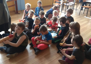 Dzieci siedzą z instrumentami podzieleni na grupy, tworzą orkiestrę. Pani odgrywa rolę dyrygenta.