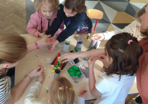 Dzieci przy stoliku łączą elementy, by powstał wielkanocny zajączek.