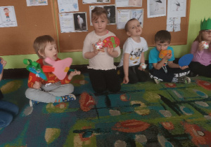 Dzieci siedzą na dywanie i prezentują swoje prace.