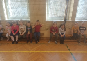 Dzieci siedzą w sali gimnastycznej.