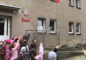 Dzieci wskazują flagę Polski na budynku.