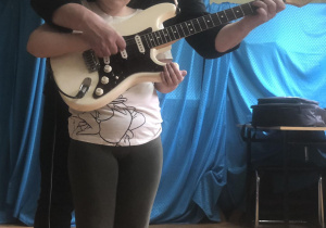 Dziewczynka z grupy czerwonej gra z pomocą gitarzysty na gitarze elektrycznej.
