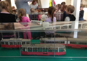 Gablota z modelami tramwajów, w tle dzieci oglądają wystawę w Muzeum.