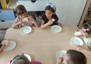 Dzieci jedzą samodzielnie przygotowane kanapeczki z serkiem smakowym.