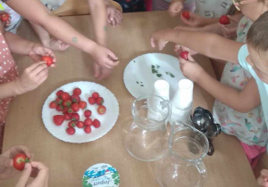 Dzieci obieraja truskawki z szypułek.