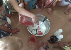 Dzieci przekładają zmiksowane truskawki do misy z jogurtem.